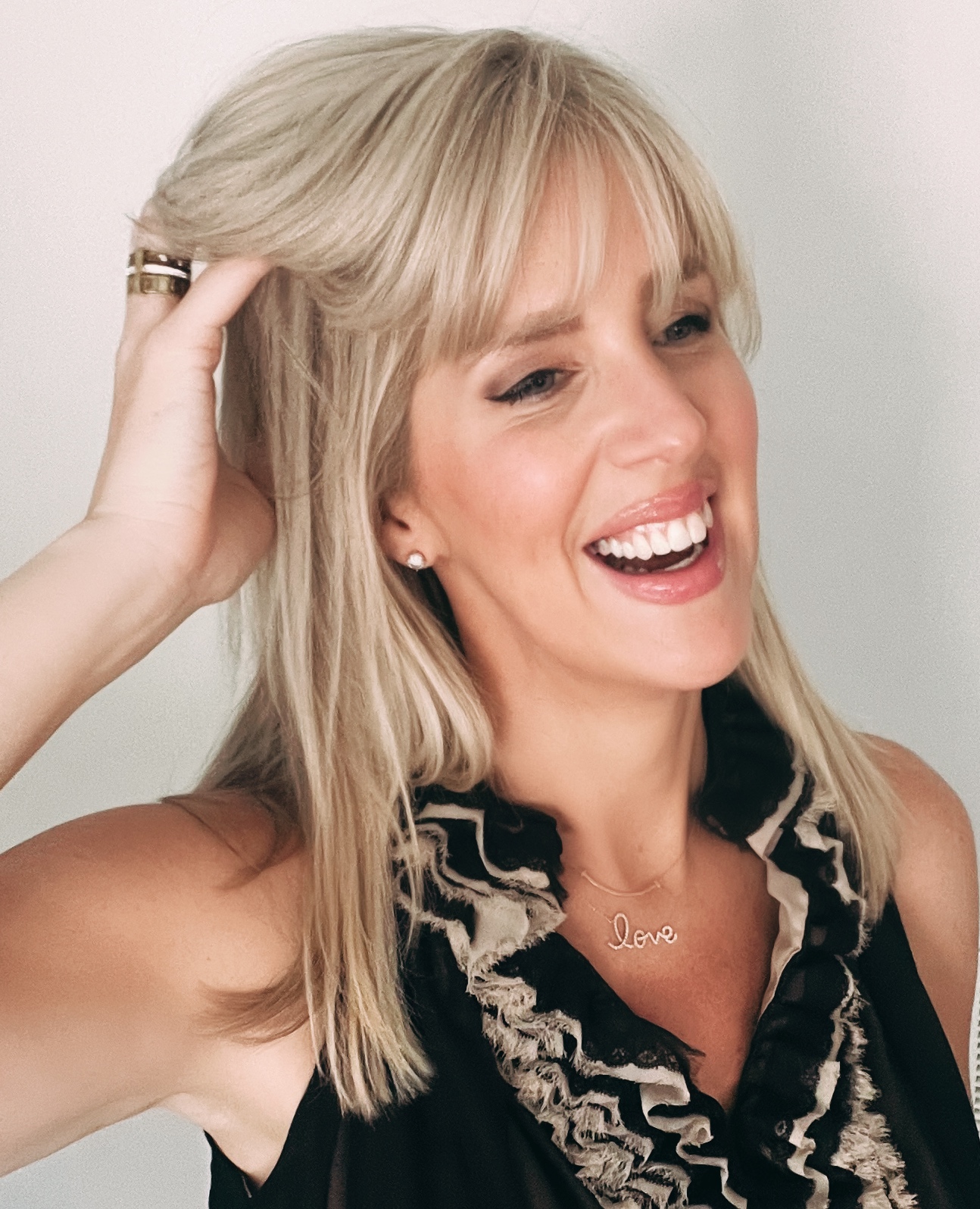 parisian style, Kelly Robbins, founder of Fifth & Paris, smiling in a chic ruffled blouse with a gold 'love' necklace.