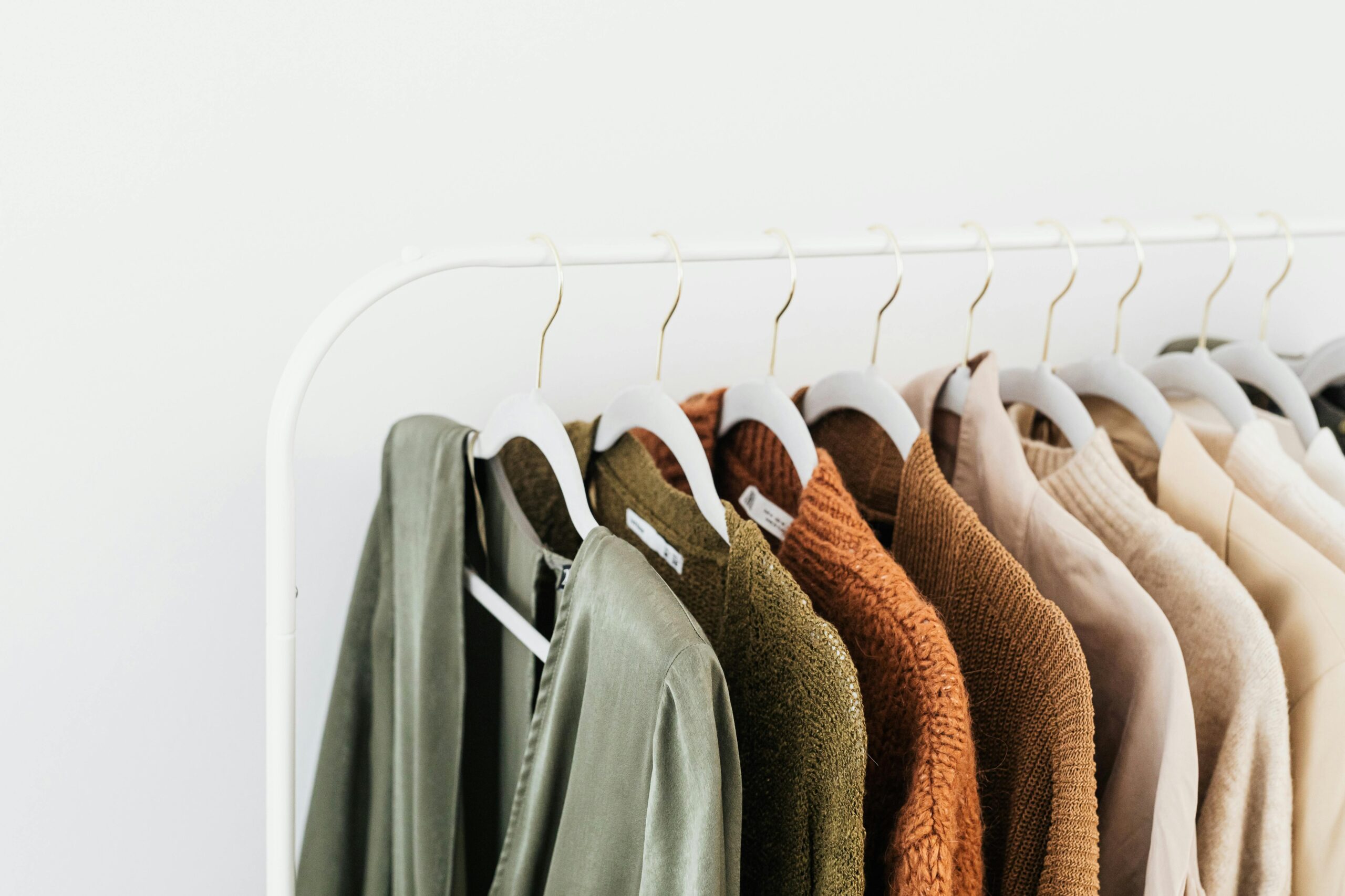 Capsule wardrobe showing neutral colors sweaters hanging on a clothing rod